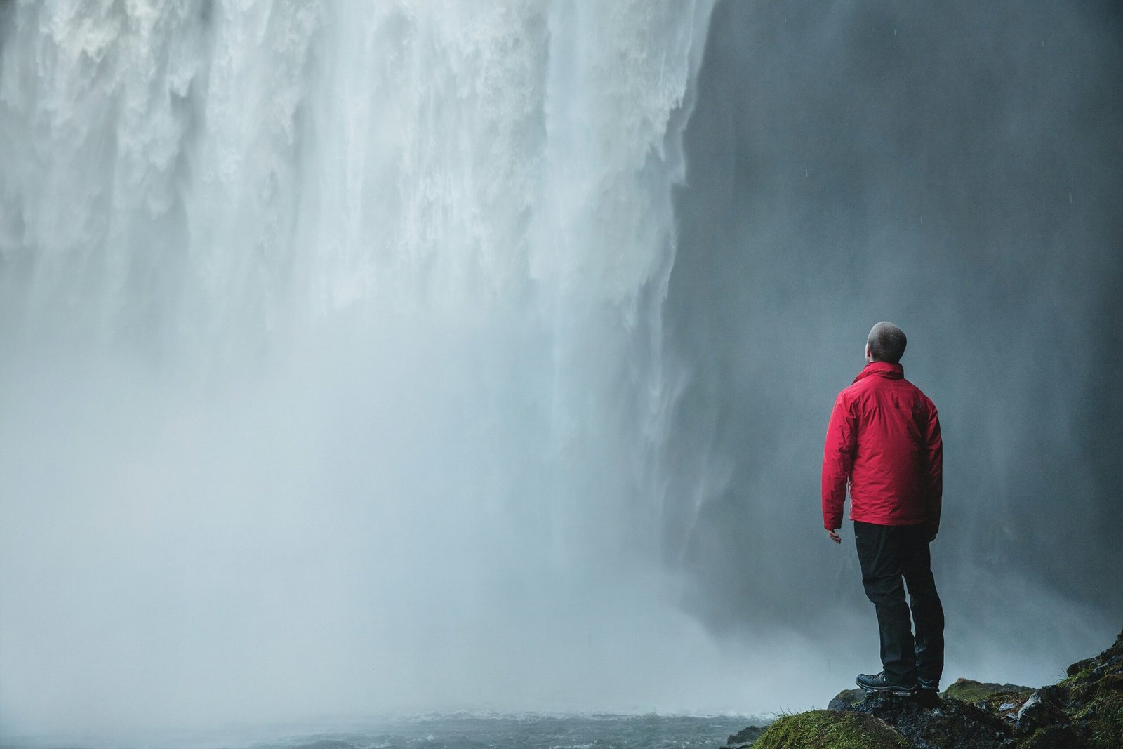 man standing on a rock facing waterfalls